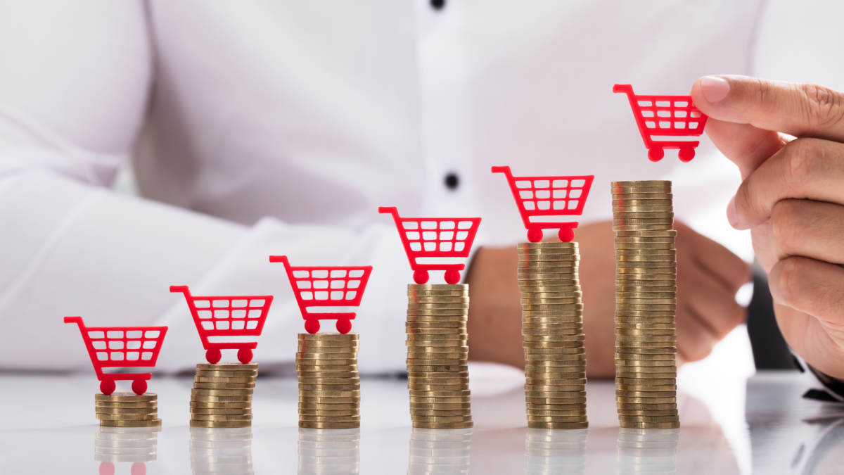 Businessperson's hand placing red shopping cart over increasing stacked coins